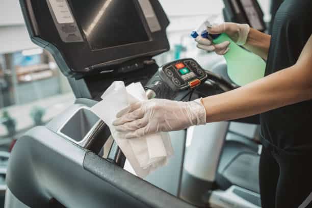 Efficient Gym Cleaning: Diligent Woman Maintains Spotless Treadmill Amidst Motivated Exercisers