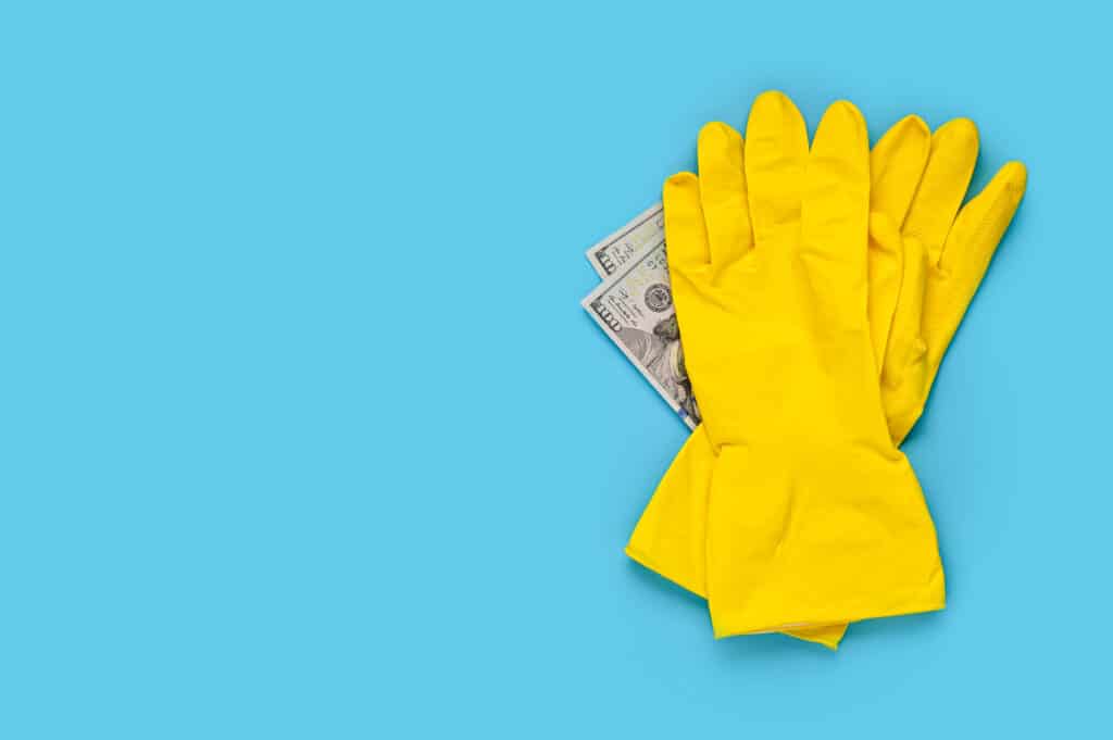 Bright yellow rubber gloves and a dollar bill rest on a vibrant blue background. Textured gloves hint at practical use, evoking a connection between manual labor and financial gain.